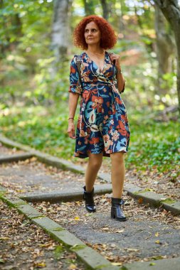 Parktaki çiçekli elbiseli güzel, kıvırcık saçlı bir kadının portresi.