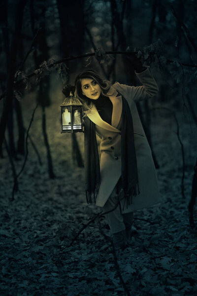 Woman with a lantern in a spooky forest at night