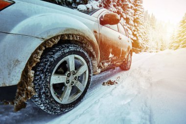 Kışın karla dolu bir arabanın geniş açılı görüntüsü, arkasında günbatımı olan bir dağ yolunda.