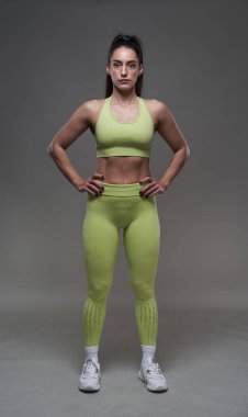 Çekici İspanyol fitness modeli gri arka planda spor kıyafetleriyle poz veriyor. 