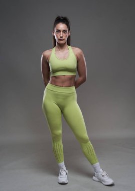 Çekici İspanyol fitness modeli gri arka planda spor kıyafetleriyle poz veriyor. 