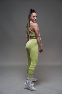 Çekici İspanyol fitness modeli gri arka planda spor kıyafetleriyle poz veriyor. 