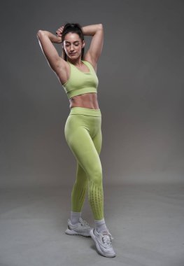 Çekici İspanyol fitness modeli gri arka planda spor kıyafetleriyle poz veriyor. 