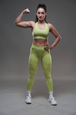 Çekici İspanyol fitness modeli gri arka planda spor kıyafetleriyle poz veriyor. 