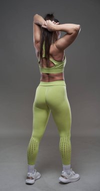 Çekici İspanyol fitness modeli gri arka planda spor kıyafetleriyle poz veriyor. 