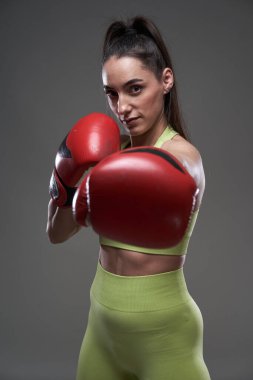 Kırmızı boks eldivenli genç bayan boksör, yumruk, gri arka plan