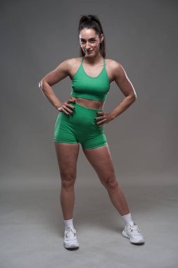 Çekici İspanyol fitness modeli gri arka planda spor kıyafetleriyle poz veriyor. 