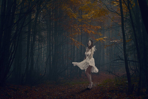 Beautiful young woman in white dress dancing in a mysterious forest in autumn colors