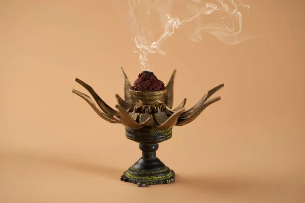 A spiritual yoga indian bronze lotus flower burning incense with white smoke, on beige background