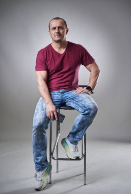 Orta yaşlı bir adamın tam boy stüdyo portresi ve gri arka planda kot pantolon, elinde cep telefonu.