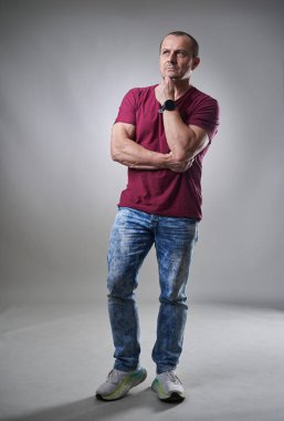 Orta yaşlı bir adamın tam boy stüdyo resmi ve gri arka planda kot pantolon, güvensizlik ifadesi.
