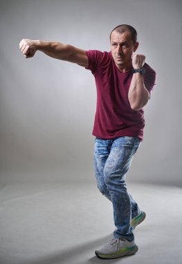 Olgun bir adamın, gri arka planda, boşluğa doğru tam boy yumruklaması.