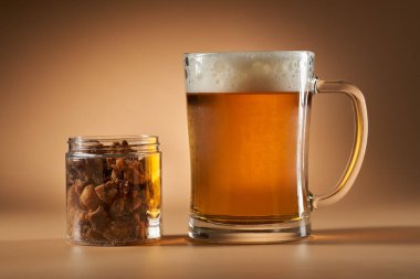 Bej arka planda izole edilmiş, soğuk bir biranın yanında cam kavanozda domuz eti.