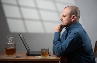 İş yerinde içki içen bir iş adamı dizüstü bilgisayarının önünde bir bardak viski içiyor.