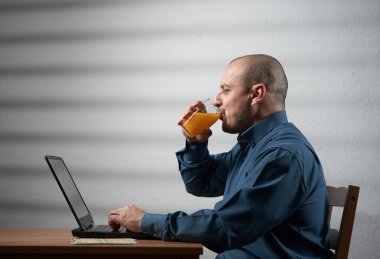 İşadamı masasında dizüstü bilgisayarla çalışırken bir bardak taze portakal suyu içiyor.