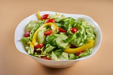 Marullu salata, vişneli domates, sarı dolma biber ve salatalık bej arka planda beyaz bir kasede.