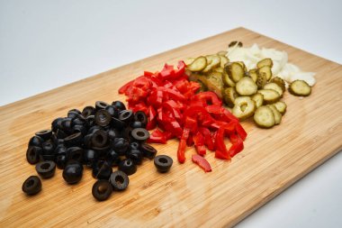 Salata için dilimlenmiş sebzeler, siyah zeytin, kırmızı salamura biber, turşu ve taze soğan, ahşap bir tahtanın üzerinde.