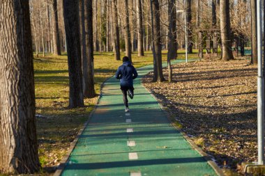 Soğuk, güneşli bir kış gününde parkta koşan bir sporcunun arkası.
