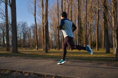 Soğuk ve güneşli bir kış gününde parkta koşan kulaklıklı olgun bir sporcu.
