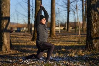 Soğuk, güneşli bir kış gününde koşmadan önce ısınan ve esneyen olgun bir koşucu.