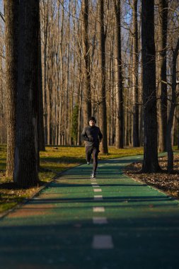 Soğuk ve güneşli bir kış gününde parkta koşan kulaklıklı olgun bir sporcu.