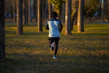 Soğuk, güneşli bir kış gününde parkta koşan bir sporcunun arkası.