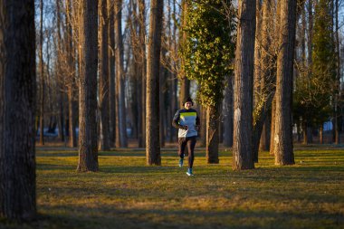 Soğuk ve güneşli bir kış gününde parkta koşan kulaklıklı olgun bir sporcu.