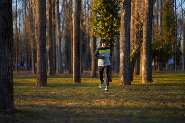 Soğuk ve güneşli bir kış gününde parkta koşan kulaklıklı olgun bir sporcu.