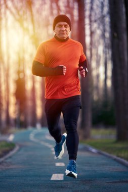 Atletik bir adam soğuk bir kış gününde gün batımında parkta koşar.