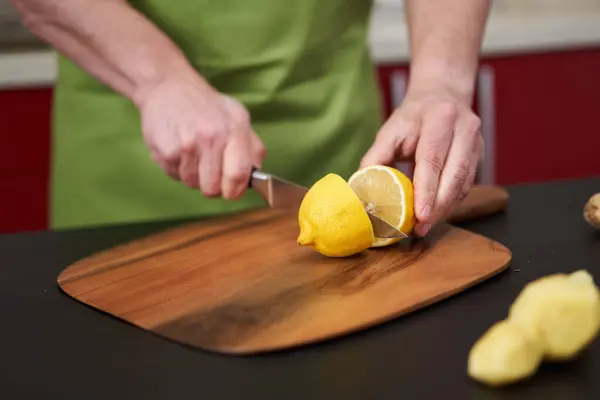 Chef\'s hands cutting a lemon in half on a wooden board