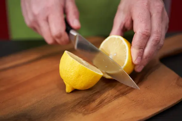 Chef\'s hands cutting a lemon in half on a wooden board