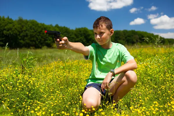 Portrait of a child holding a toy gun on a field of celandine, Ranunculus ficaria,