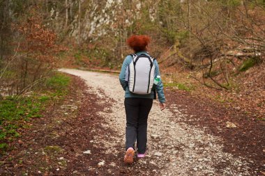 Sırt çantalı bir kadın ormanda, dağlarda tek başına yürüyüş yapıyor.