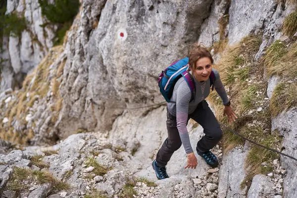 登山者妇女爬上安全线上陡峭的墙 免版税图库图片