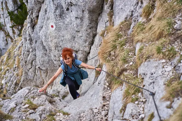 登山者妇女爬上安全线上陡峭的墙 免版税图库照片