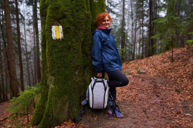 Yağmurlu bir günde dağlarda sırt çantalı bir kadın yürüyüş yapıyor.