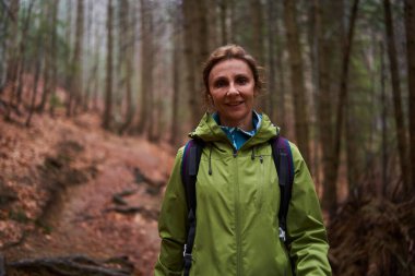 Yağmurlu bir günde dağlarda sırt çantalı bir kadın yürüyüş yapıyor.