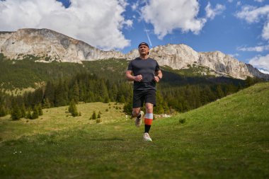 Yetişkin adam patikası dağlarda, çimlerin üzerinde koşuyor.