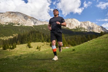 Yetişkin adam patikası dağlarda, çimlerin üzerinde koşuyor.