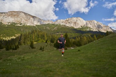 Yetişkin adam patikası dağlarda, çimlerin üzerinde koşuyor.