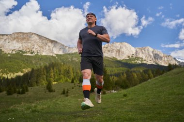 Yetişkin adam patikası dağlarda, çimlerin üzerinde koşuyor.