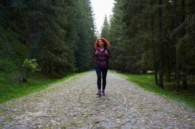 Sırt çantalı bir kadın dağdaki çam ormanında yürüyüş yapıyor.