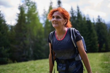 Sırt çantalı bir kadın dağdaki çam ormanında yürüyüş yapıyor.