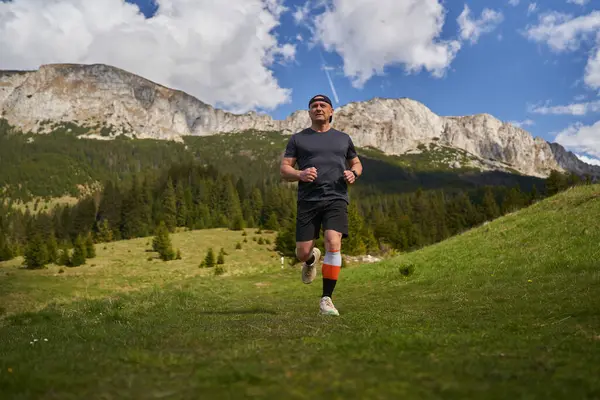 Yetişkin adam patikası dağlarda, çimlerin üzerinde koşuyor.