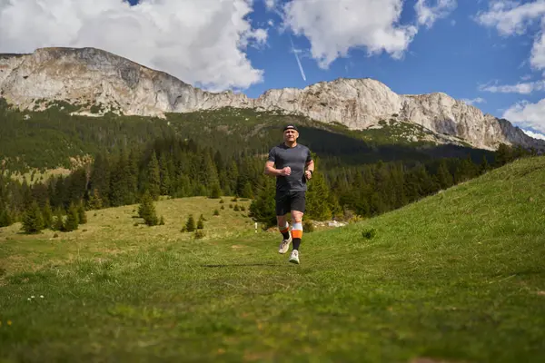 Yetişkin adam patikası dağlarda, çimlerin üzerinde koşuyor.