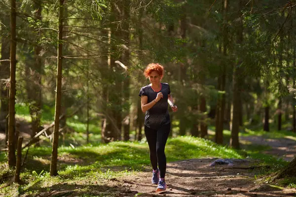 レッドヘッドの女性トレイルランナーのトレーニング 森林ランニングの丘 ロイヤリティフリーのストック画像