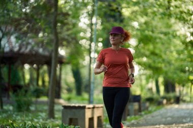 Kızıl saçlı atletik kadın koşucu parkta koşuyor. 