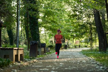 Atletik formda bir kadın gündüz parkta koşuyor. 