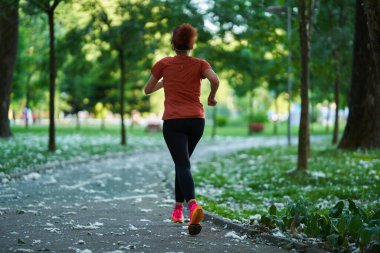 Atletik formda bir kadın gündüz parkta koşuyor. 