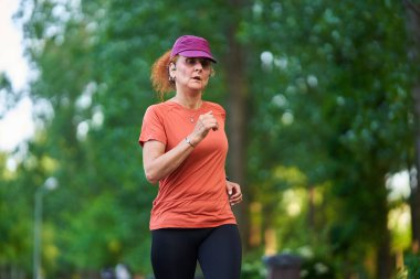 Atletik zinde bir kadın koşucu parkta koşuyor.